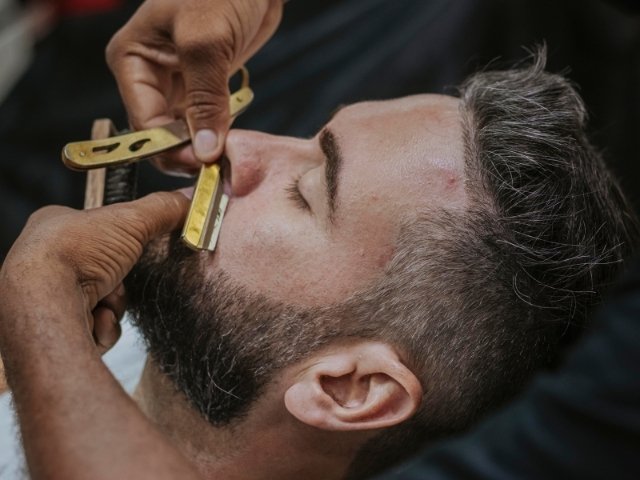 Profissional de barbearia fazendo a barba do seu cliente com navalha